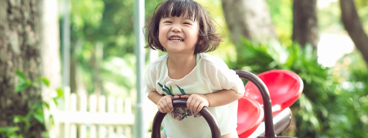 A young Asian girl smiling and enjoying herself on a playground